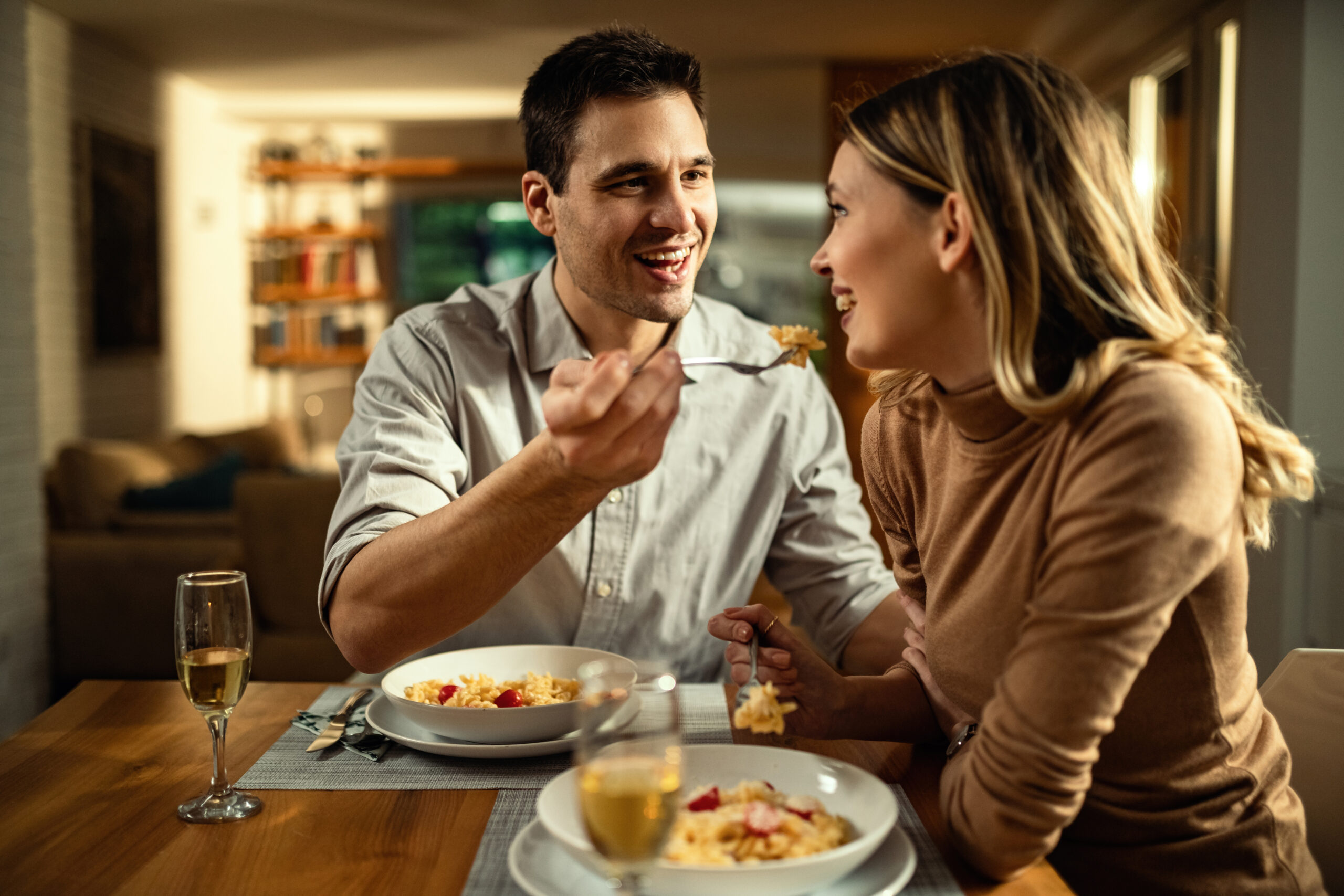 A couple sharing a romantic dinner at home, with wine glasses, candlelight, and a cozy atmosphere.