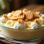 Homemade banana pudding in a large serving dish with layers of pudding, bananas, and vanilla wafers, topped with whipped cream and wafer crumbs.